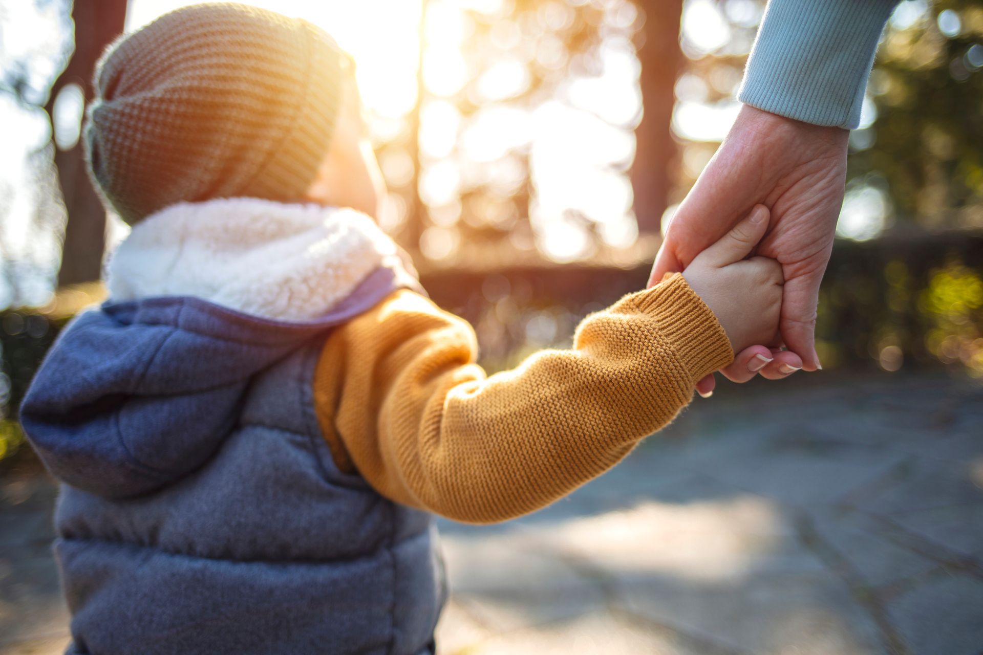 Child holding an adult's hand, walking outside in the sunlight.