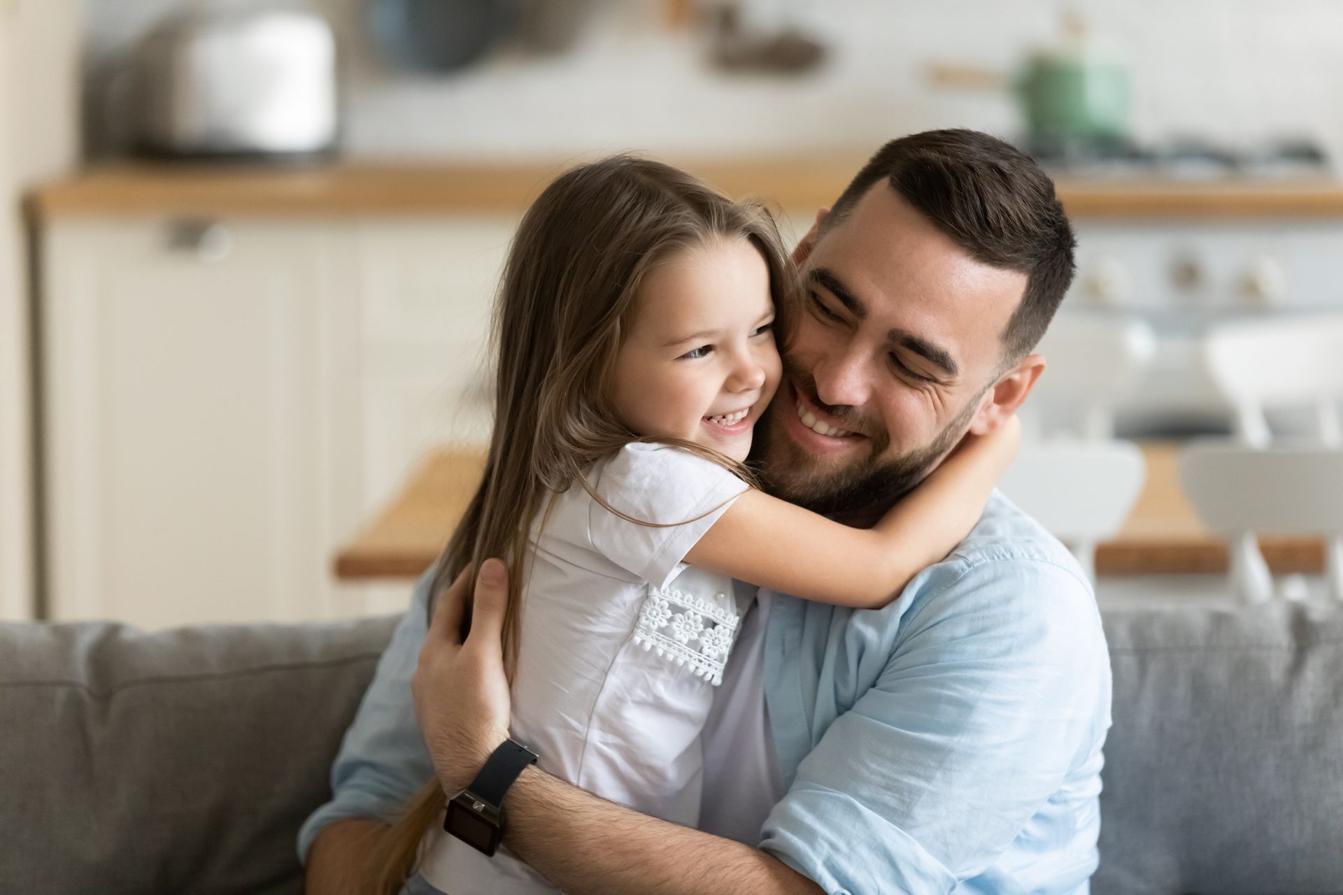 Father embracing his young daughter, both smiling in a living room.