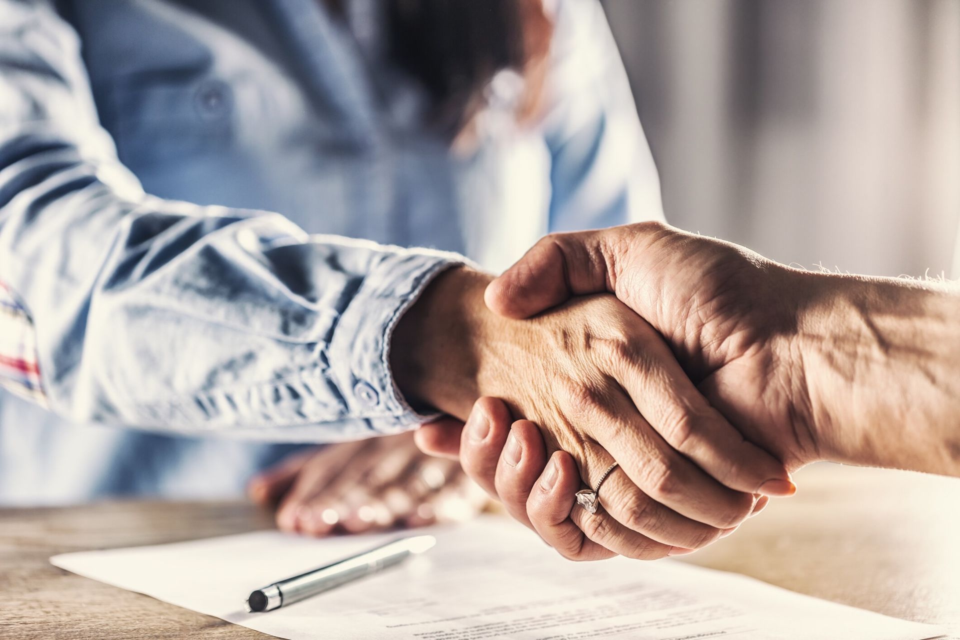 Two people shaking hands over a document on a wooden table; a deal is made.