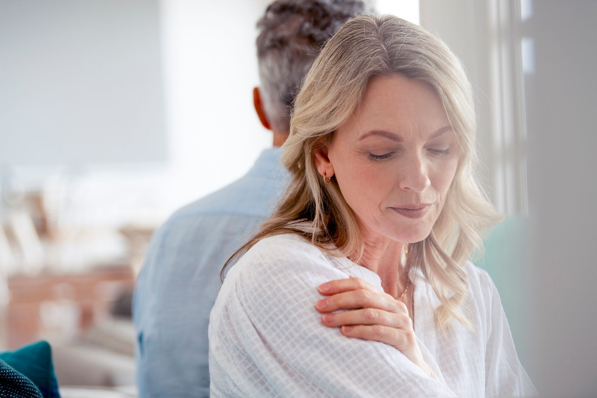Woman in white robe, facing forward with eyes closed, arms crossed. Man behind her, their backs turned.