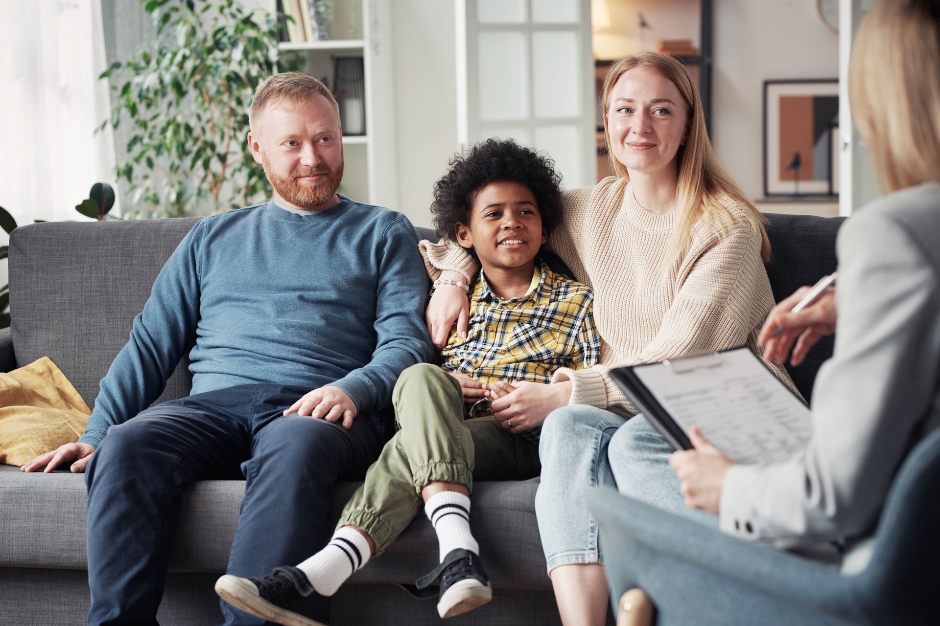 Family of three on a couch, smiling, with a therapist holding a clipboard.