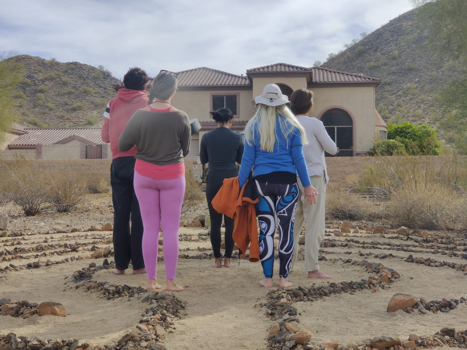 A group of people are walking through a labyrinth in front of a house