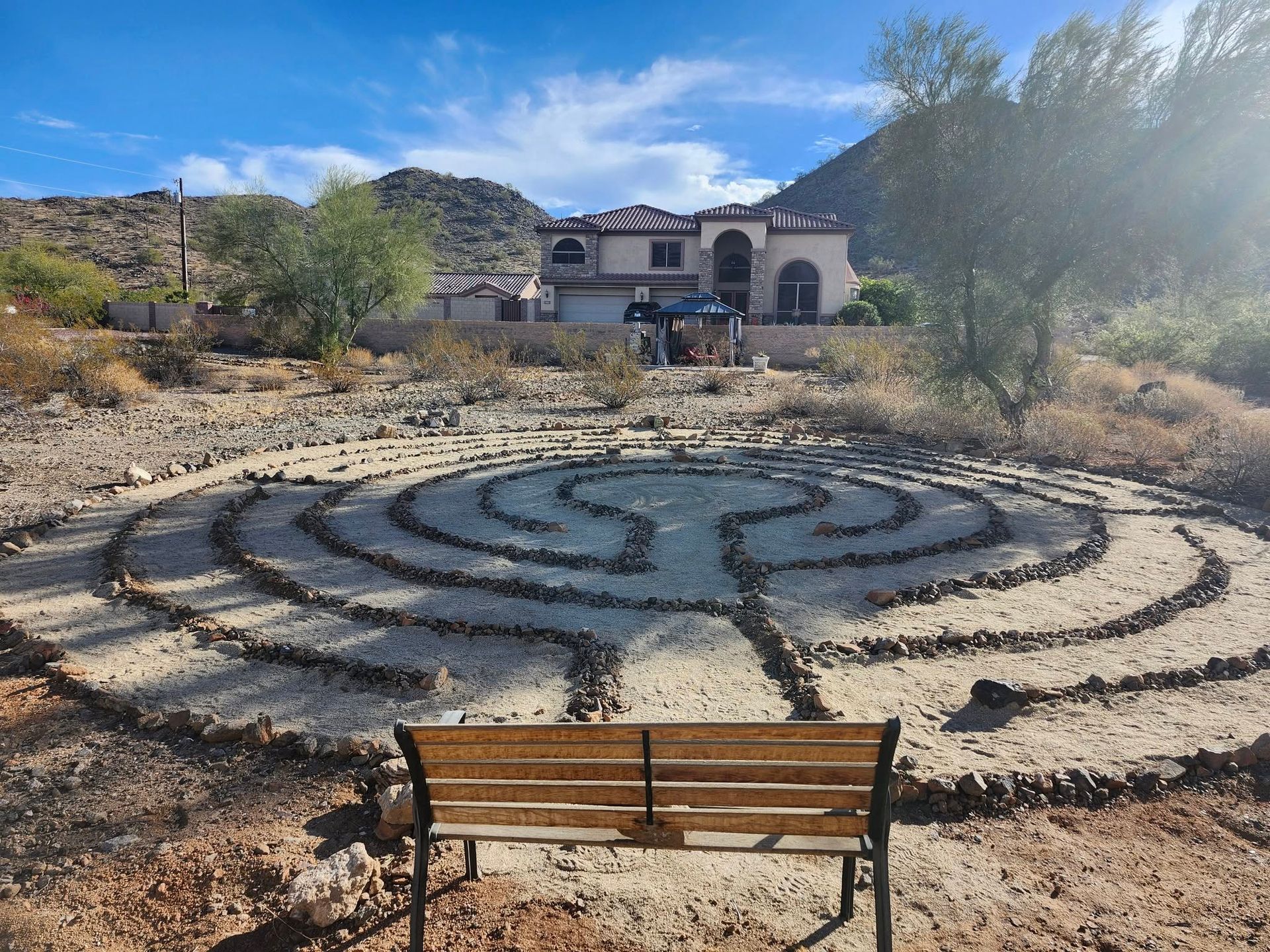 A wooden bench is sitting in front of a labyrinth with a house in the background.
