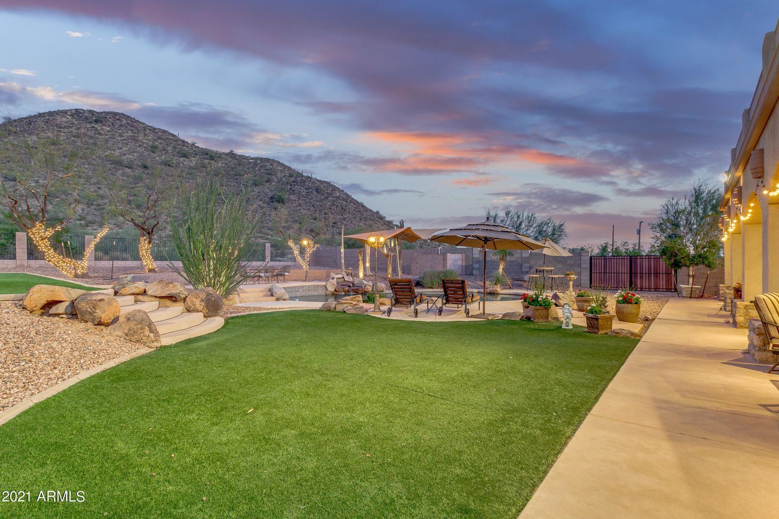 A large lawn with umbrellas and chairs in front of a house with a mountain in the background.