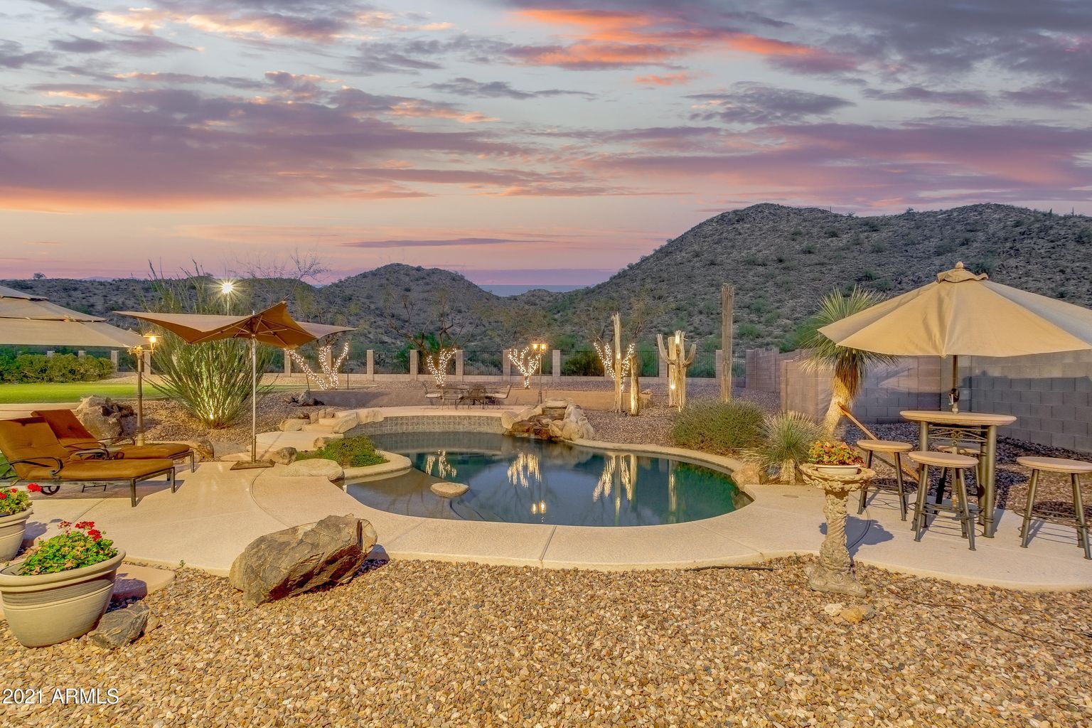 A large swimming pool surrounded by umbrellas and chairs with mountains in the background.