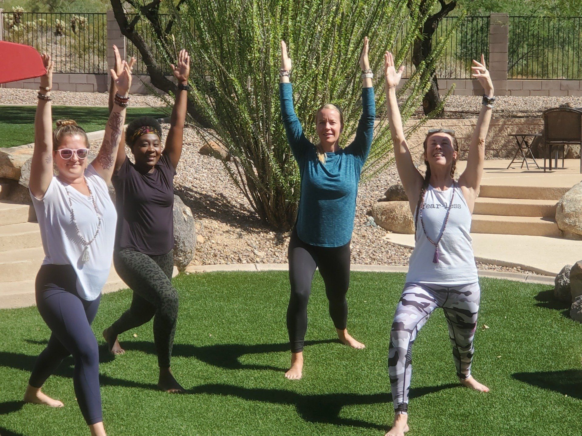 A group of women are doing yoga in a park with their arms in the air.