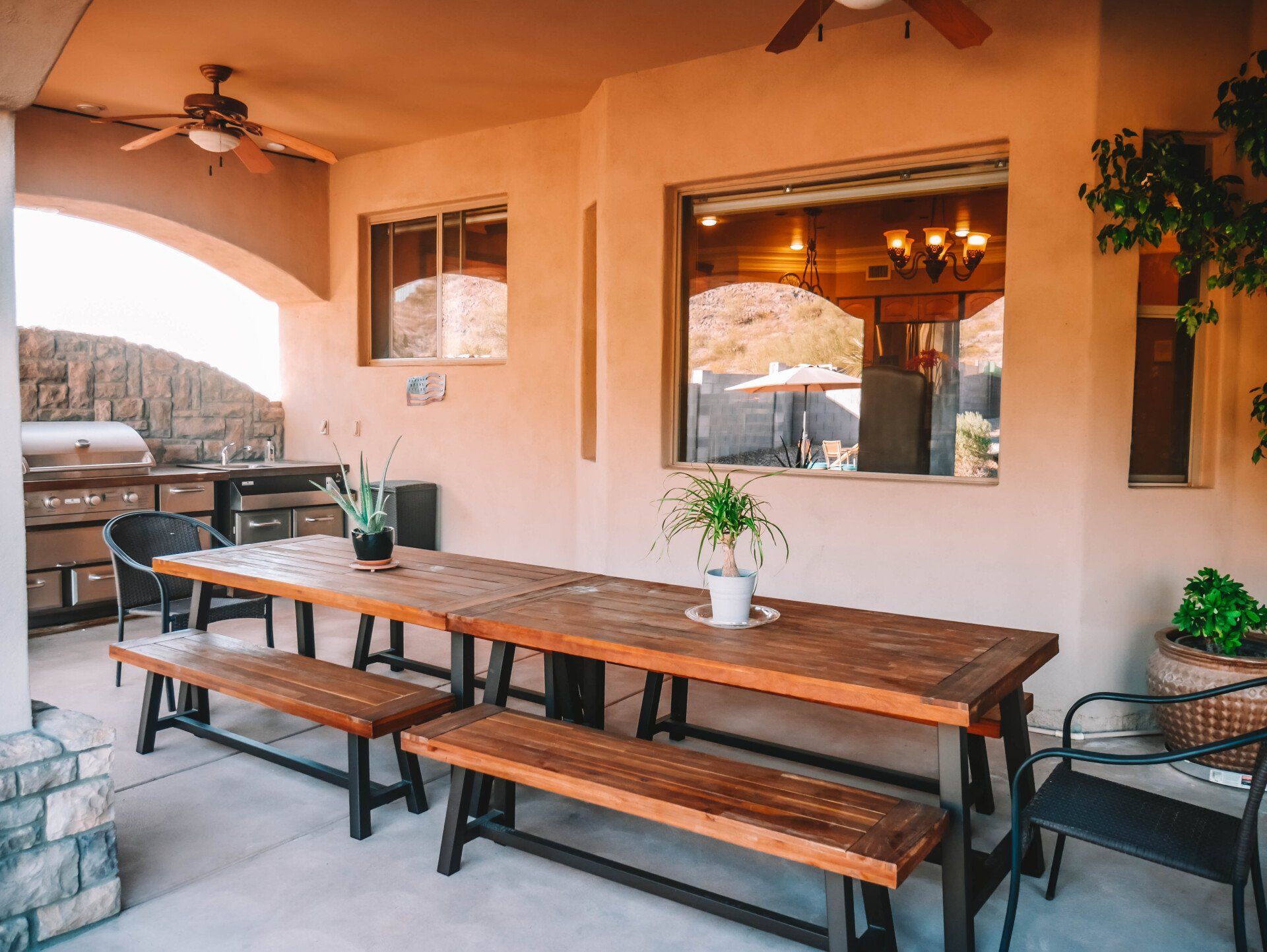 A wooden table and benches on a patio with a ceiling fan.