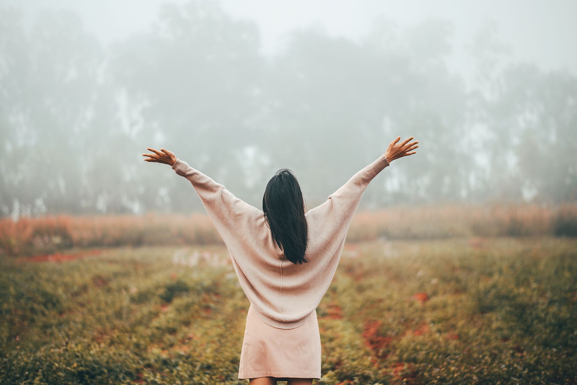 A woman is standing in a field with her arms outstretched.