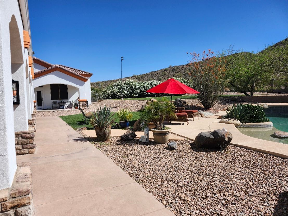 A large swimming pool surrounded by rocks and umbrellas in a backyard.