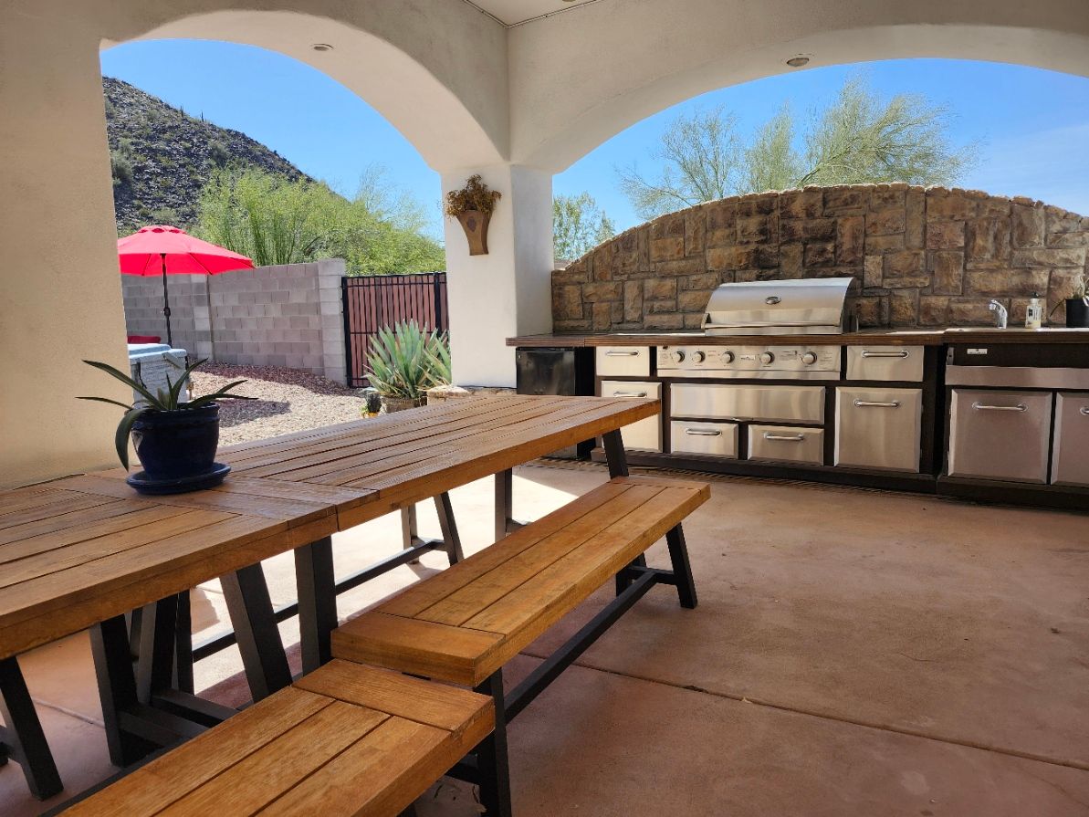 A wooden table and benches on a patio with a ceiling fan.