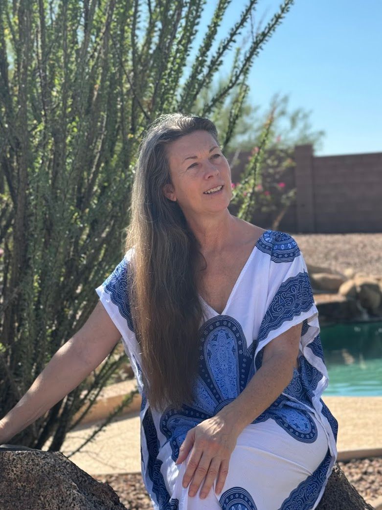 A woman in a blue and white dress is sitting on a rock near a pool.
