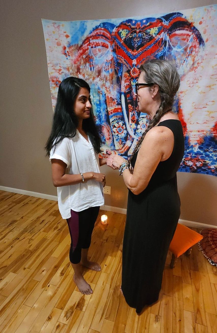 Two women are standing next to each other on a wooden floor in front of a painting of an elephant.