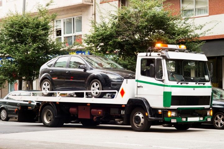 A small black car is loaded onto the back of a white with green tow truck