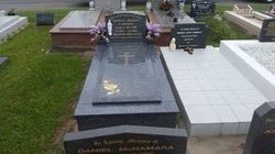 Grave with black granite headstone and cross, surrounded by other tombstones and green grass — Mackay Monumental Masons In Glenella, QLD