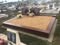 A rectangular headstone with brown trim, gravel fill, and two dark plaques in a cemetery — Mackay Monumental Masons In Glenella, QLD