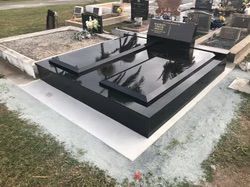 Black granite double tombstone in a cemetery, reflecting trees; gray gravel and green grass surrounding — Mackay Monumental Masons In Glenella, QLD