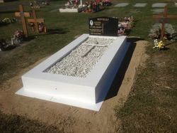 White tombstone with gravel, cross, and black headstone in a cemetery — Mackay Monumental Masons In Glenella, QLD
