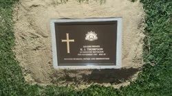 Bronze grave marker with cross, Australian coat of arms, and inscription on a bed of sand within green grass — Mackay Monumental Masons In Glenella, QLD