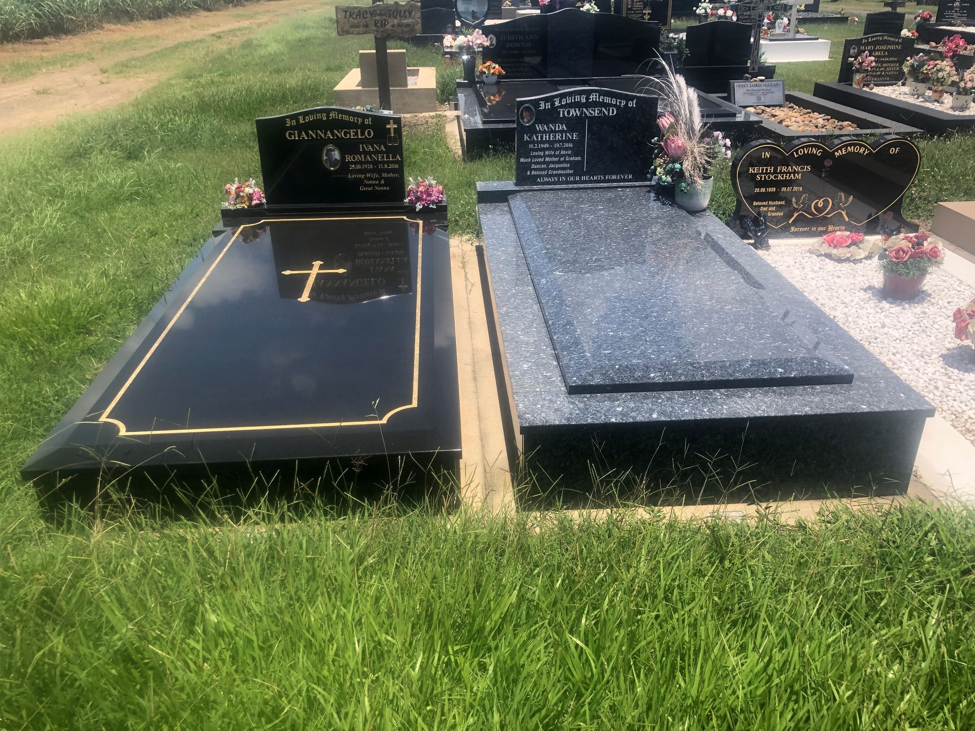 Two black granite headstones with gold trim and a cross in a grassy cemetery.