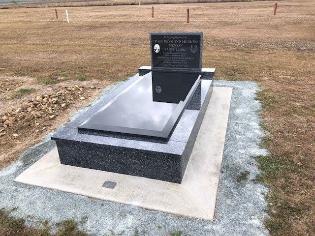 Black granite headstone with a rectangular, reflective top, set on a gray stone base in a grassy field.