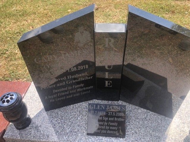 Black granite headstone with family name, dates, and inscriptions; set outdoors with a vase.