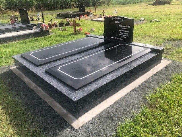 Grave with black headstone, two black grave covers, set on a gray base, in a grassy cemetery.