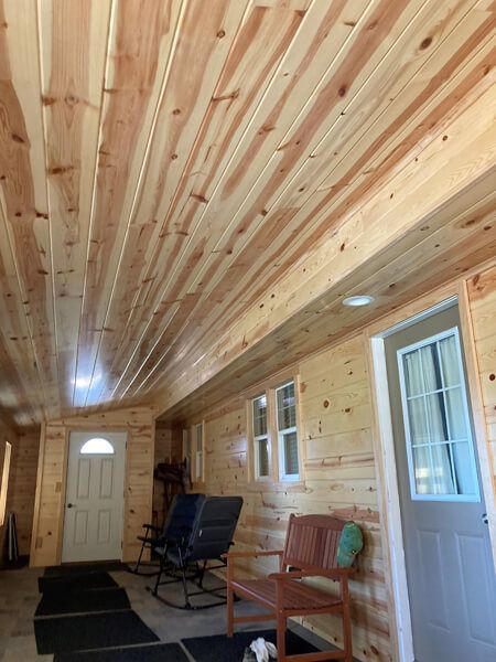 Wooden ceiling and walls in a room, two doors, small windows, chairs, and natural light.