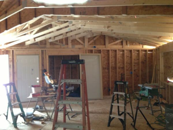 Interior of a building under construction, showing wooden framing and roof trusses. Ladders and tools are scattered throughout the space.