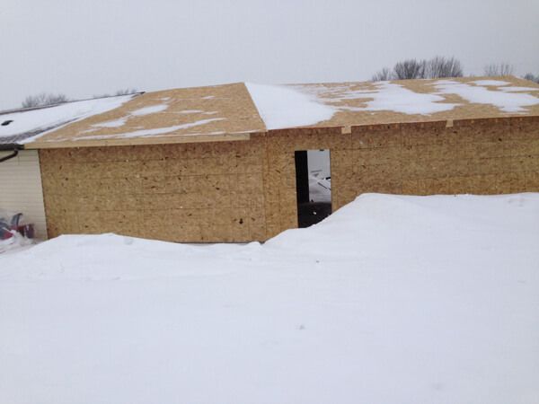 Construction of a building in the snow. Plywood walls and roof, a doorway, snow covered ground.