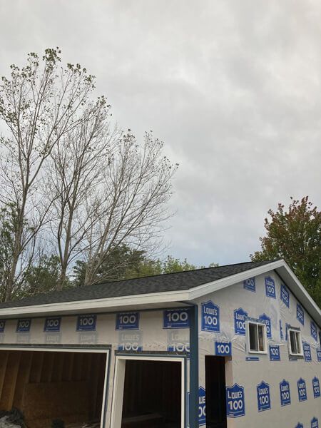 Garage under construction, wrapped in blue protective sheathing. A cloudy sky is overhead.