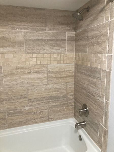 Tiled shower with a tan and beige color scheme and a white bathtub. The shower head and faucet are silver.