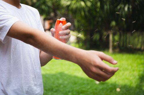 In un giardino, una persona con indosso una maglietta bianca si spruzza dell'insetticida sul braccio.