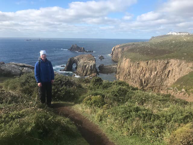 A picture of a man standing next to a cliff facing the sea