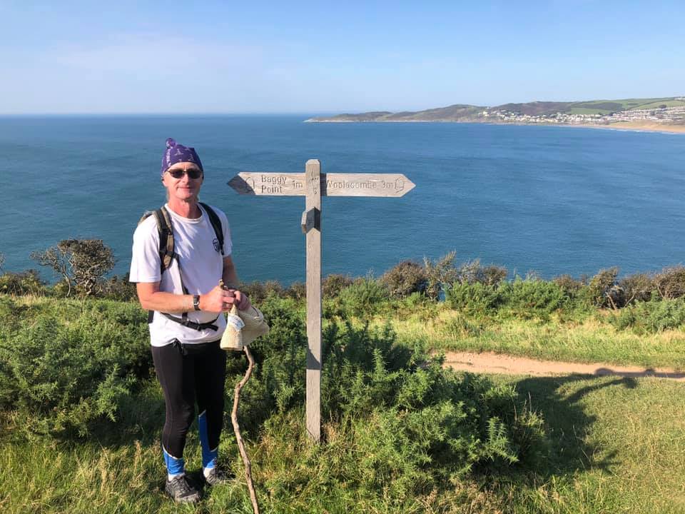 A man posing next to a sign as he is walking next to the sea