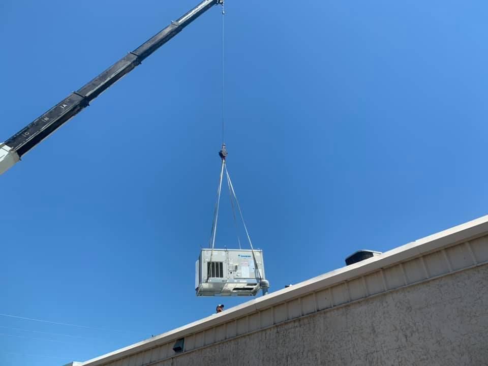 A crane is lifting a piece of equipment from the roof of a building