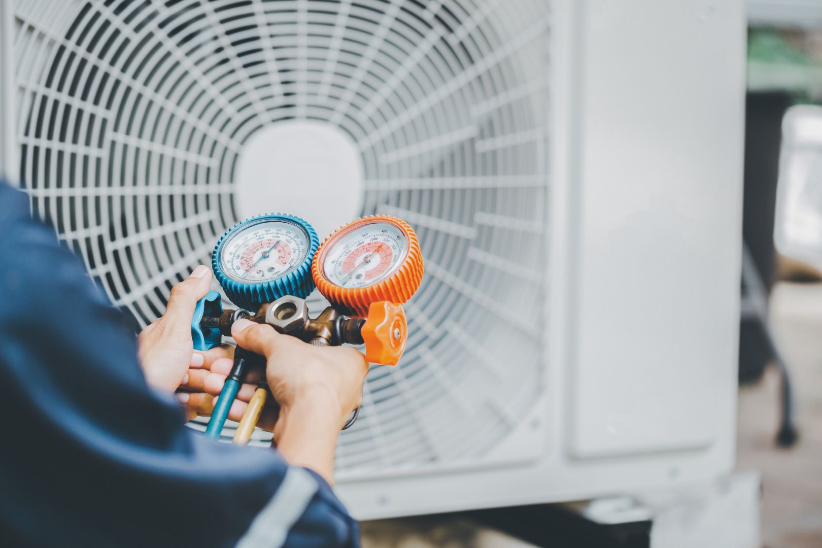 A man is working on an air conditioner with two gauges.