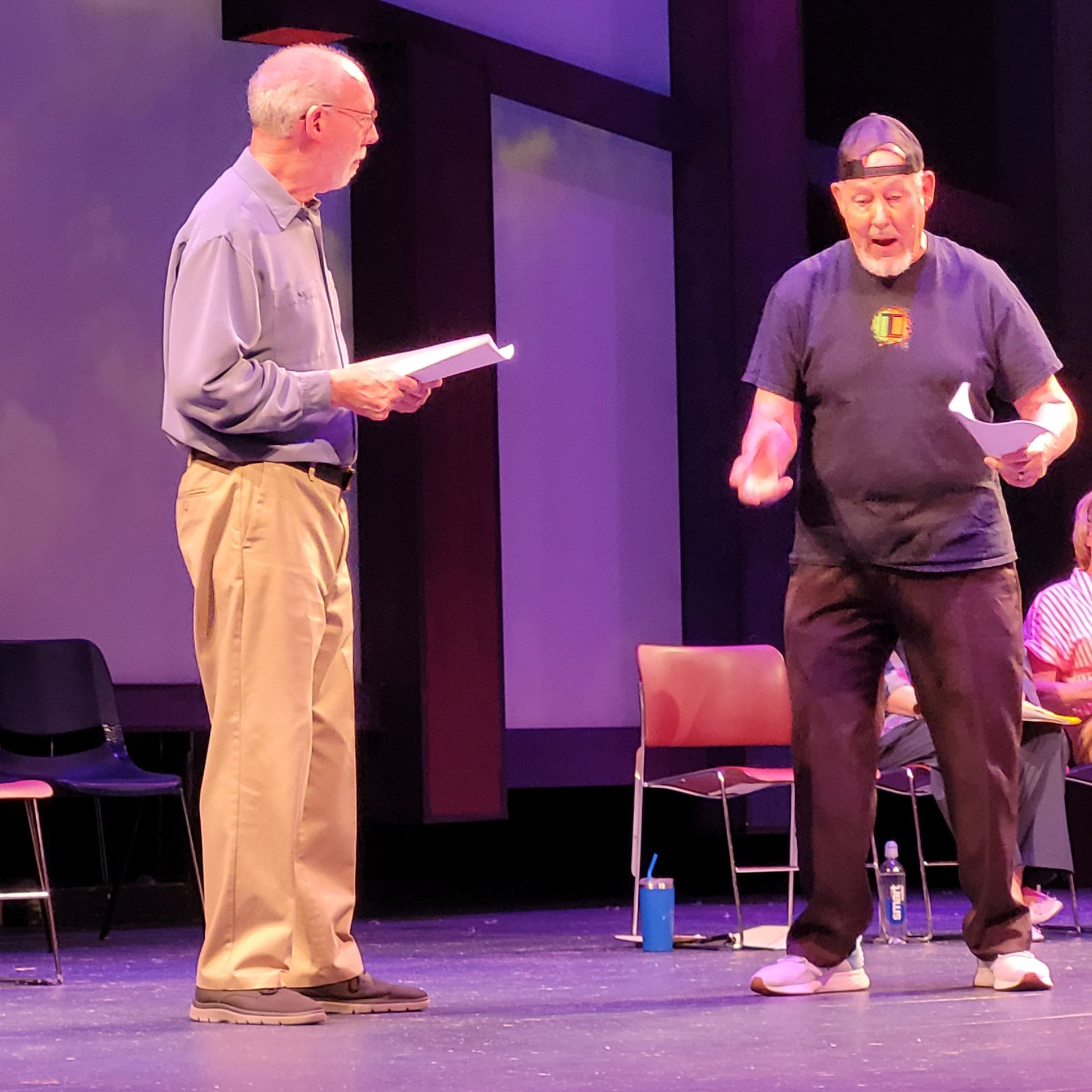 Two men standing on a stage with one wearing a black shirt with the letter g on it