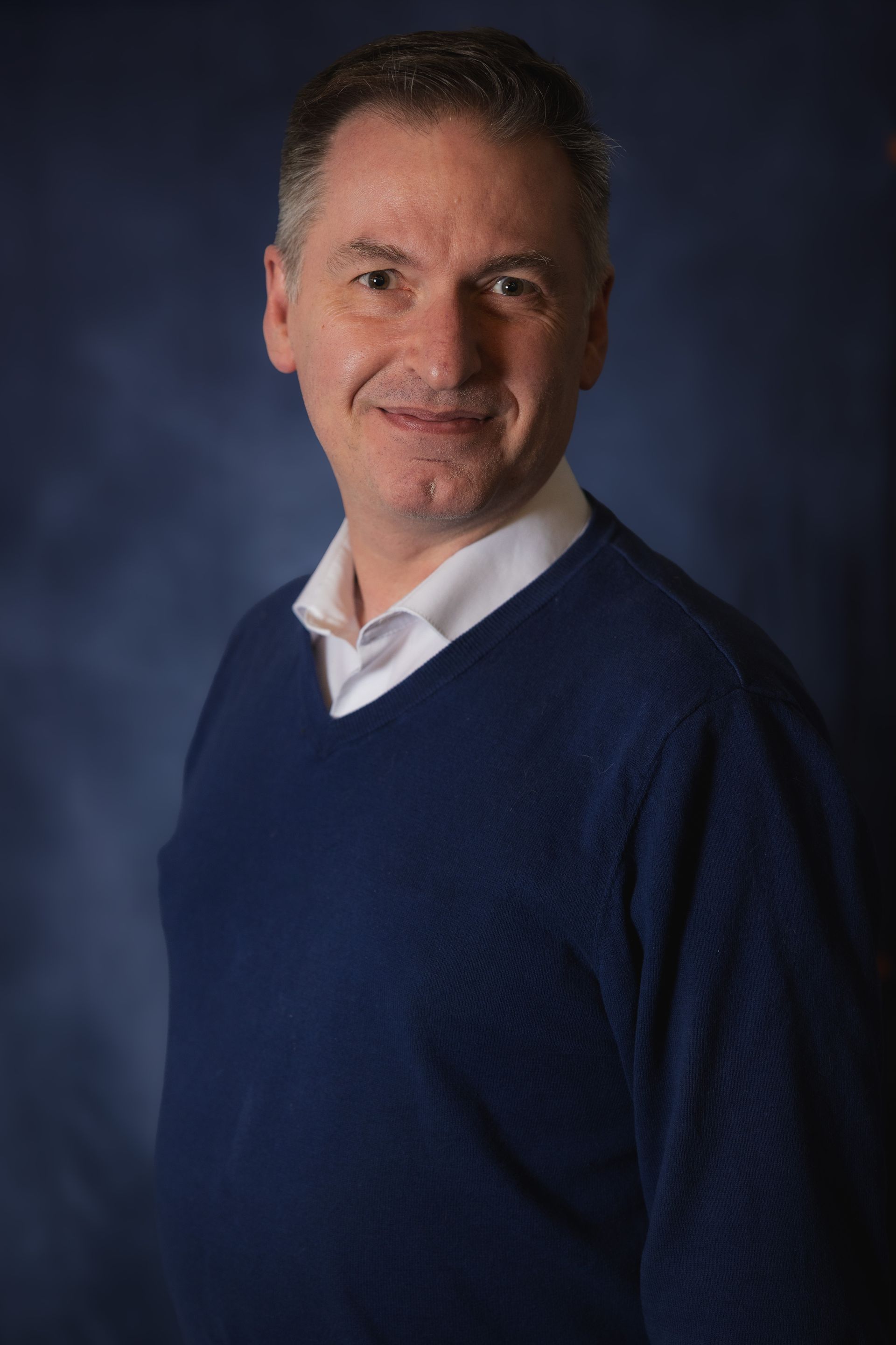 A man in a blue sweater and white shirt is smiling for the camera.