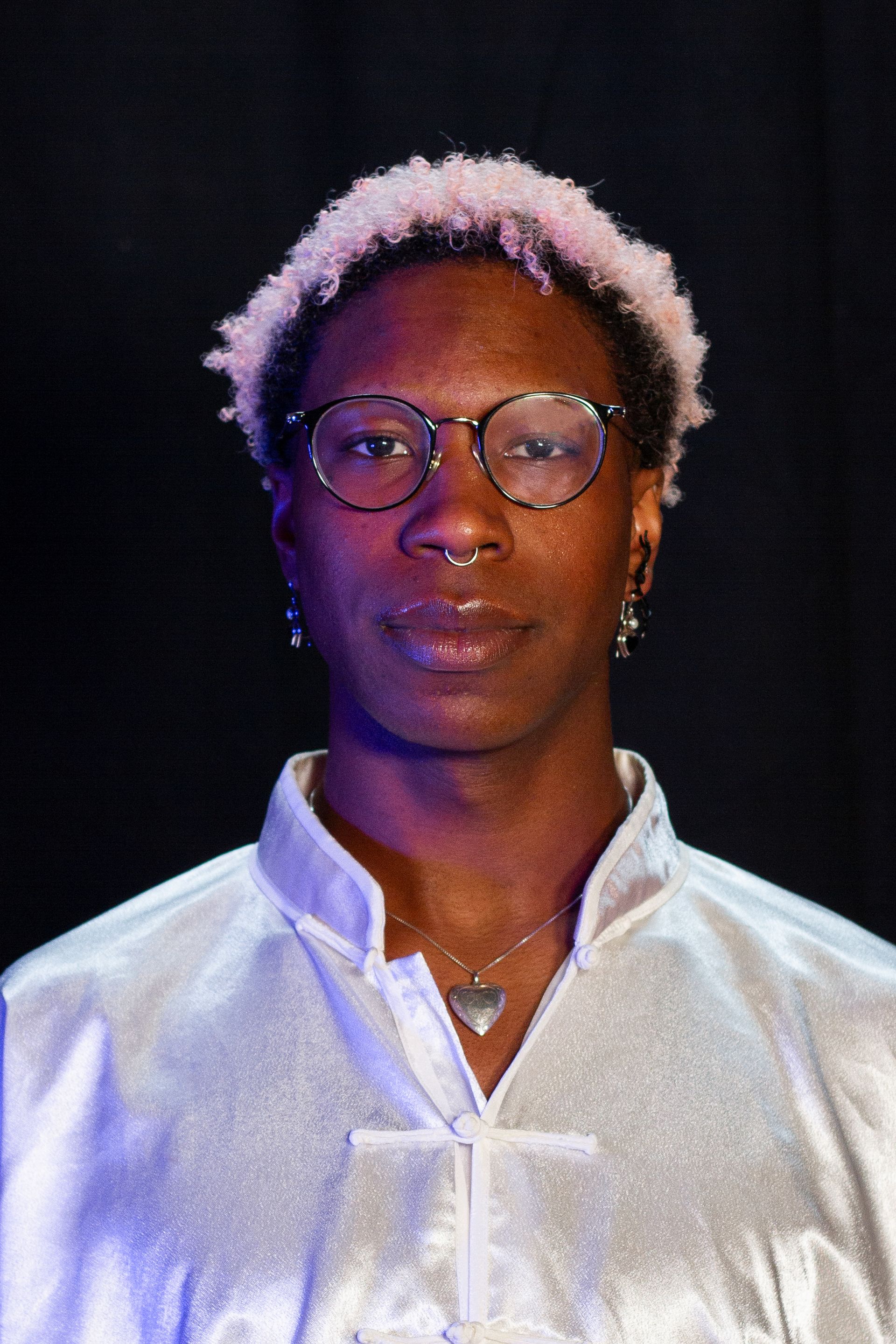 Person with pink hair, glasses, and silver shirt; looking at the camera.