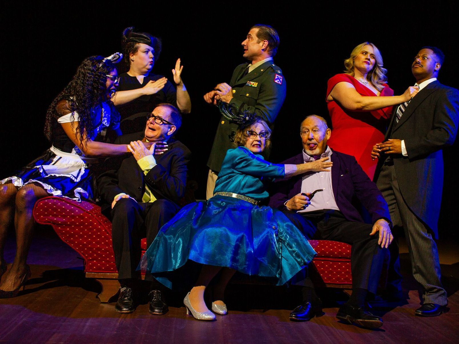 Actors in colorful costumes on stage, gesturing dramatically.