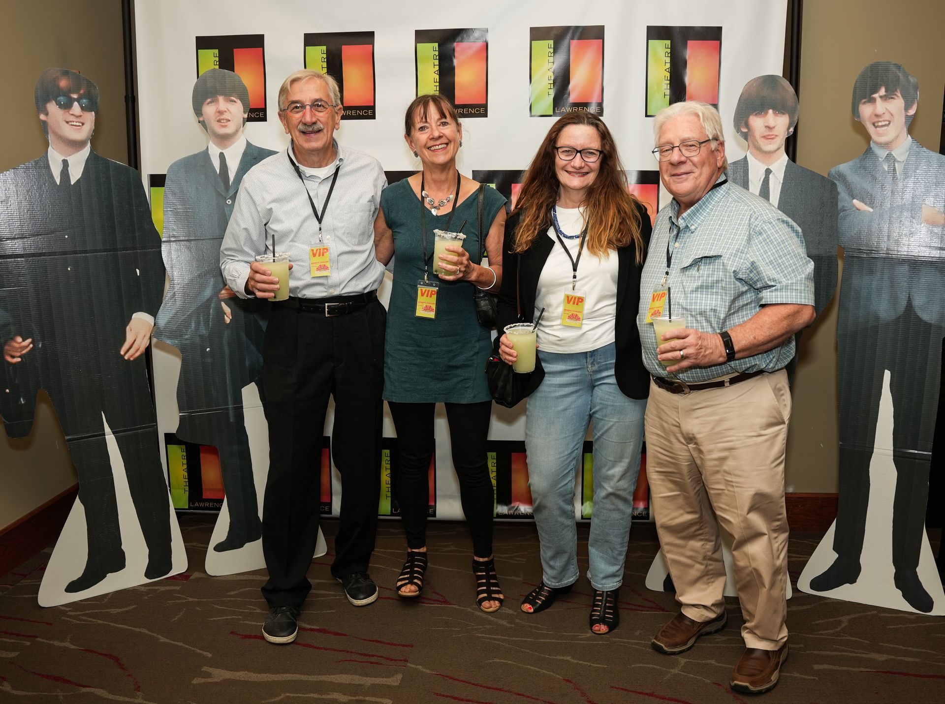 Four people pose with Beatles cutouts, holding drinks, smiling at an event.