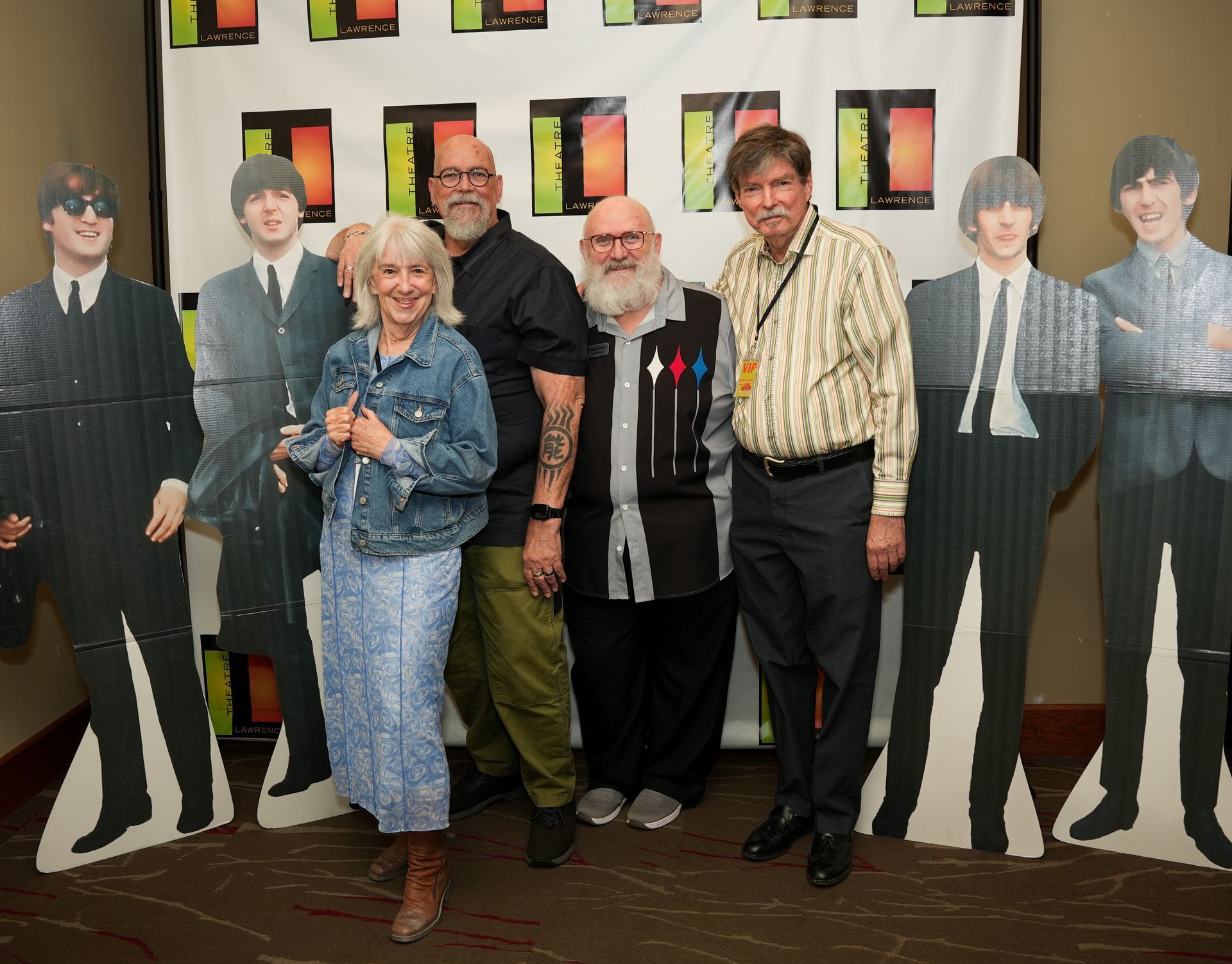 People pose with Beatles cutouts at a Beatles-themed event.