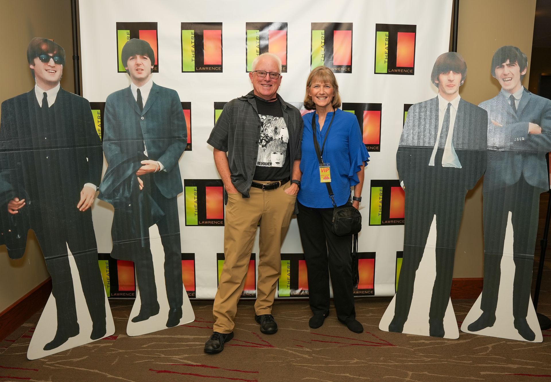 A man and woman pose with Beatles cardboard cutouts at an event.