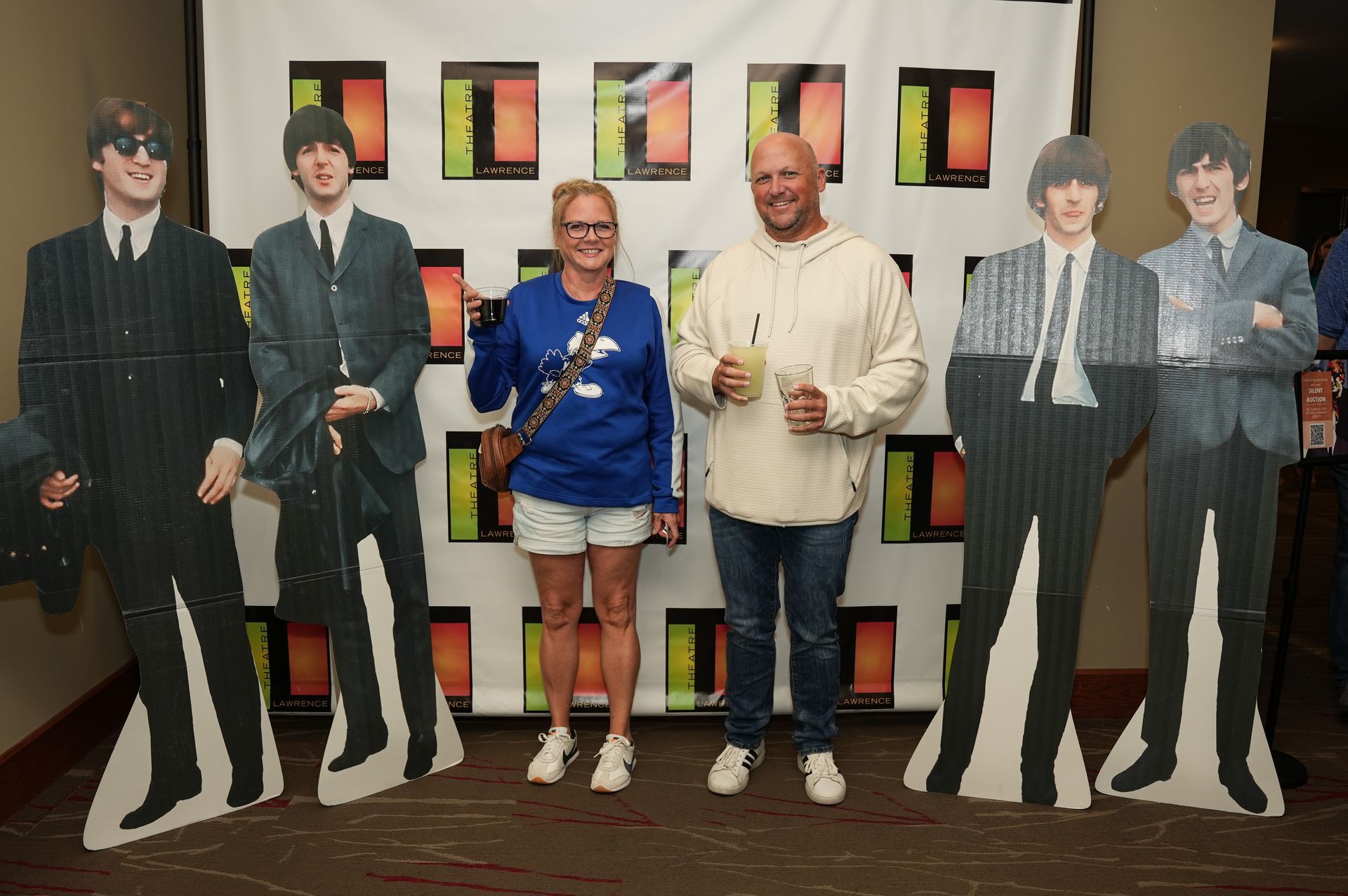 Two people pose with Beatles cardboard cutouts at an event with a colorful backdrop.