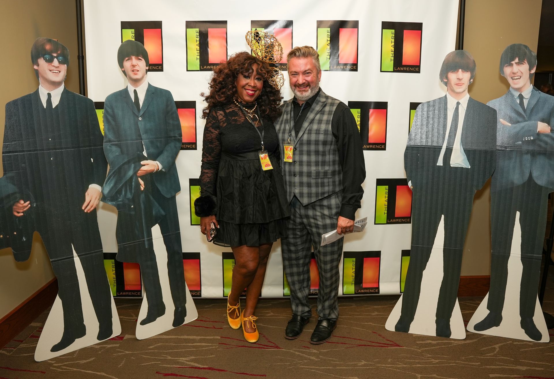 Woman and man pose with Beatles cutouts at event; black dress, checkered vest.