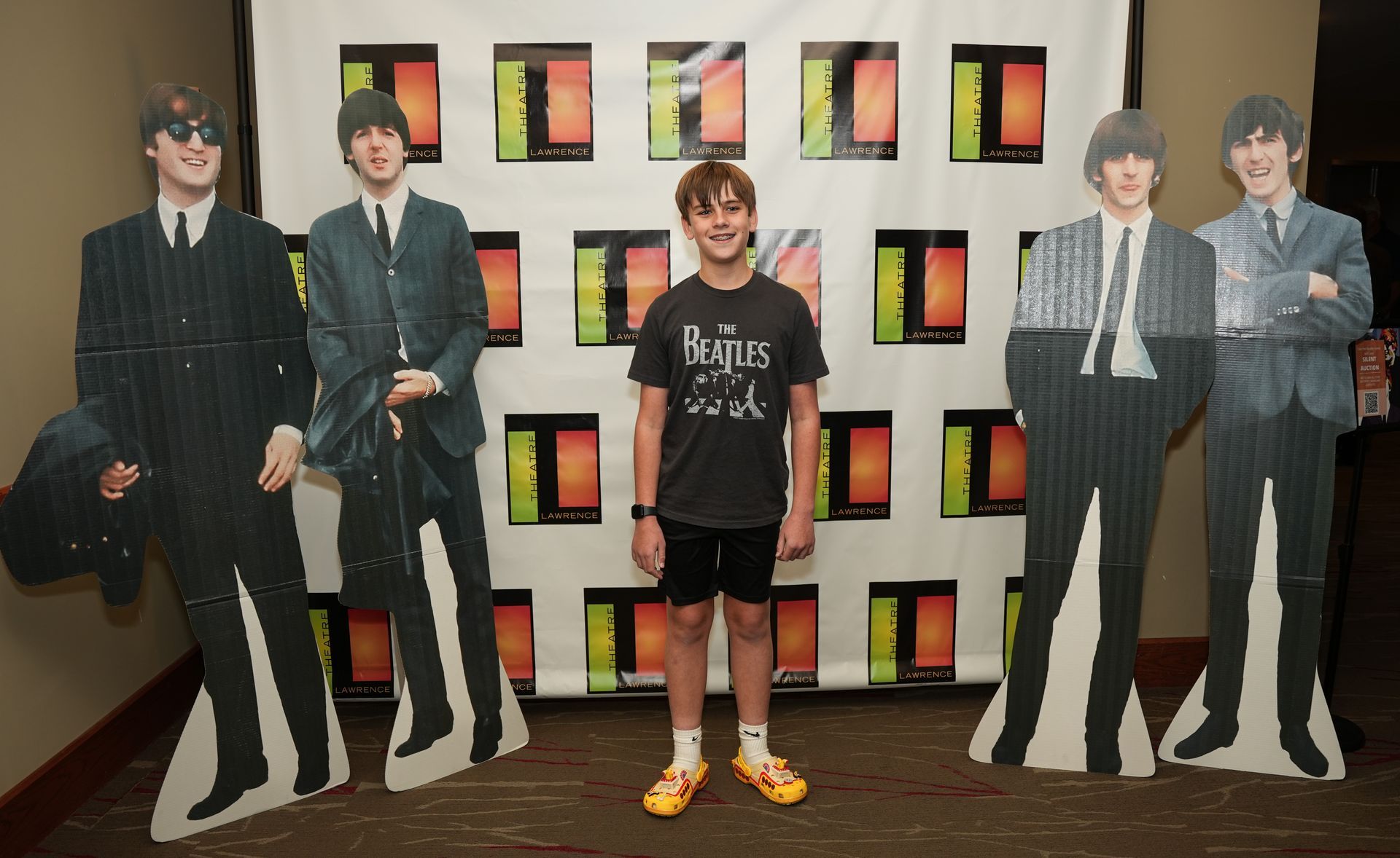 Young person posing between cardboard cutouts of The Beatles.