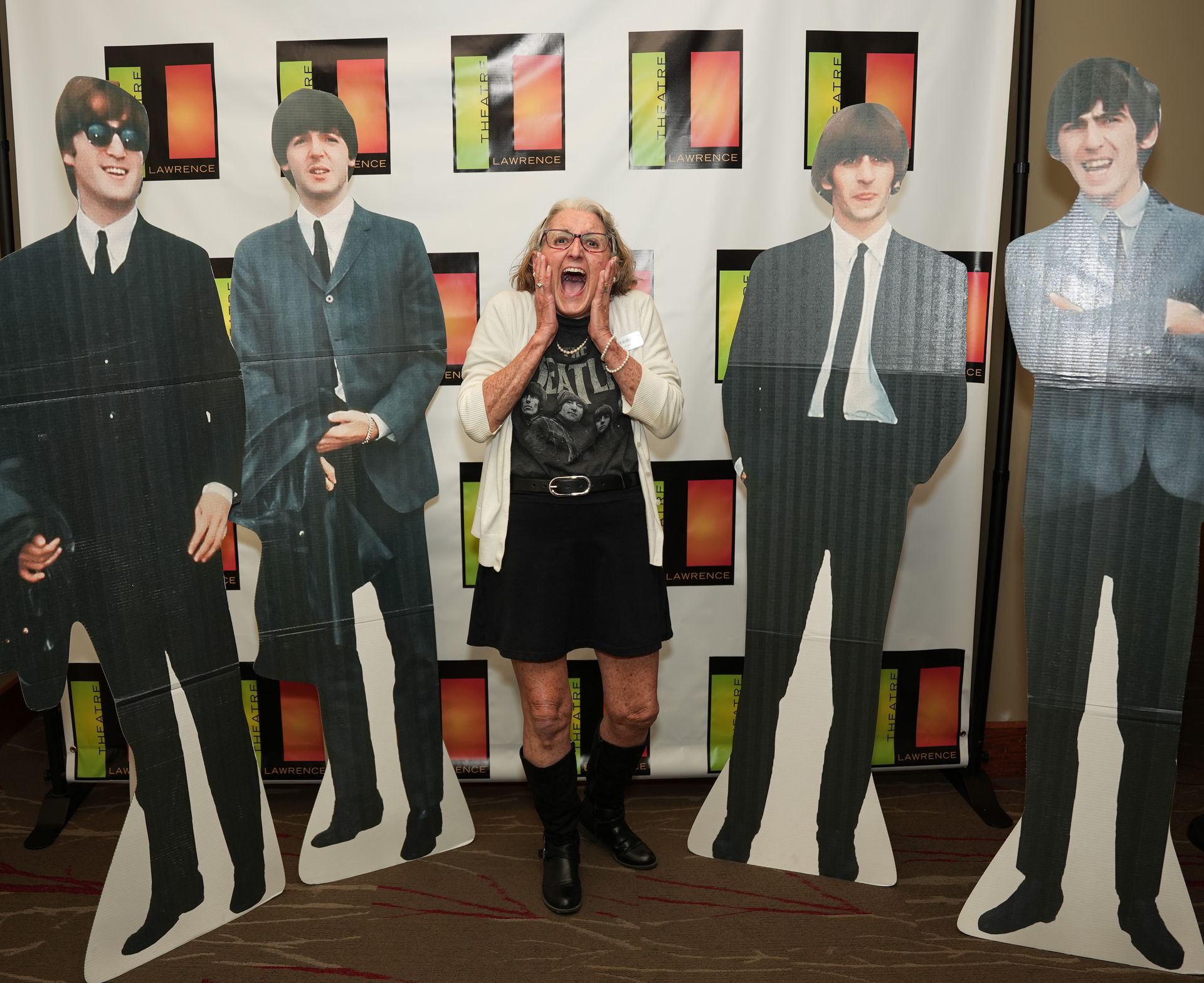 Woman shouts enthusiastically between Beatles cardboard cutouts at an event.