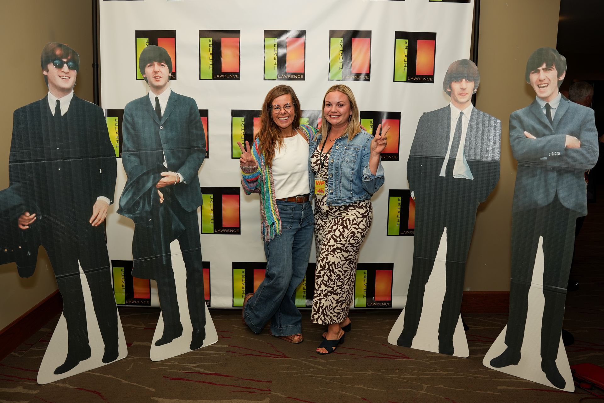 Two women pose with cardboard cutouts of The Beatles, at an event.