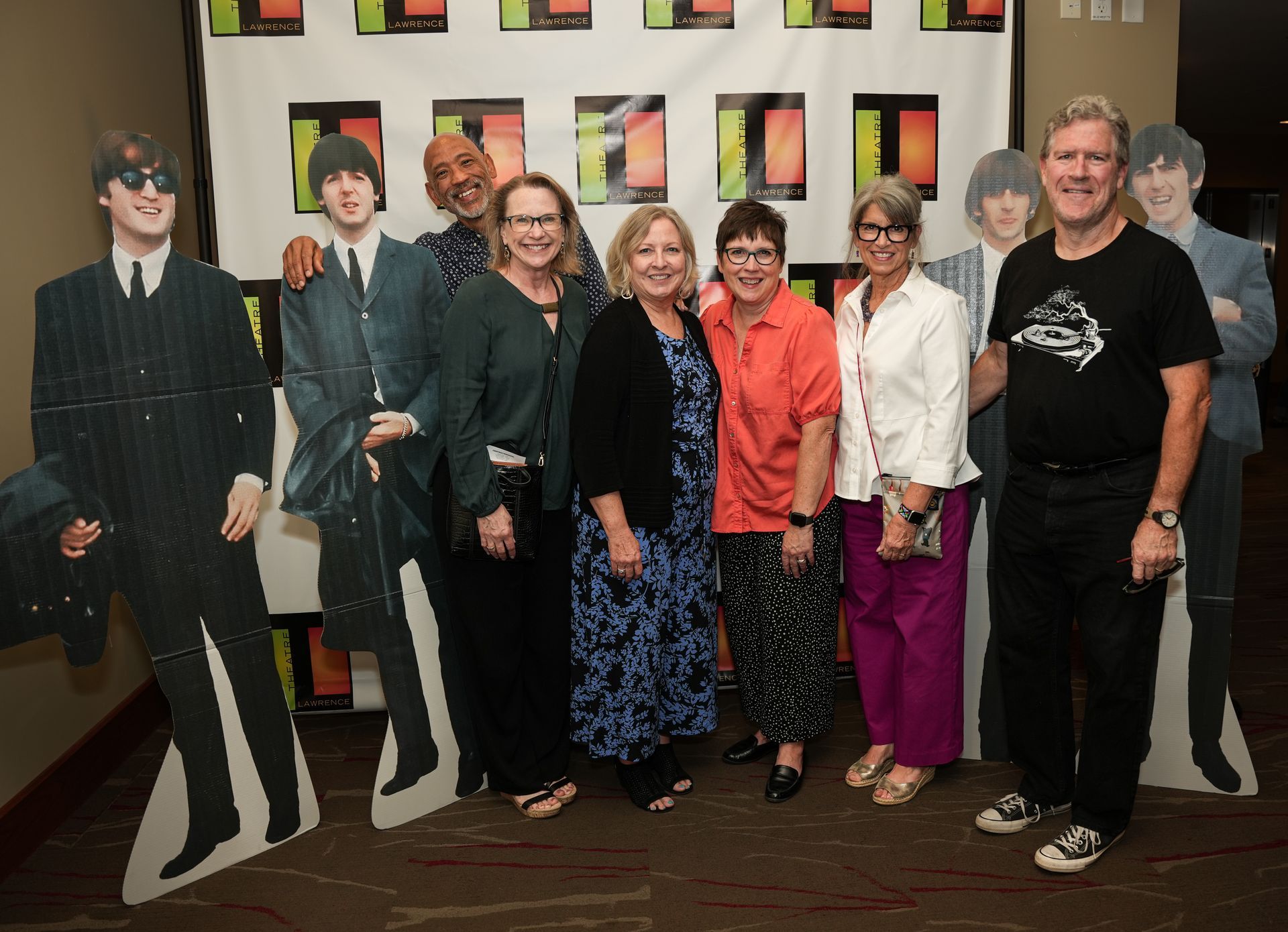 Group of people posing with Beatles cutouts, some smiling. Colorful background.