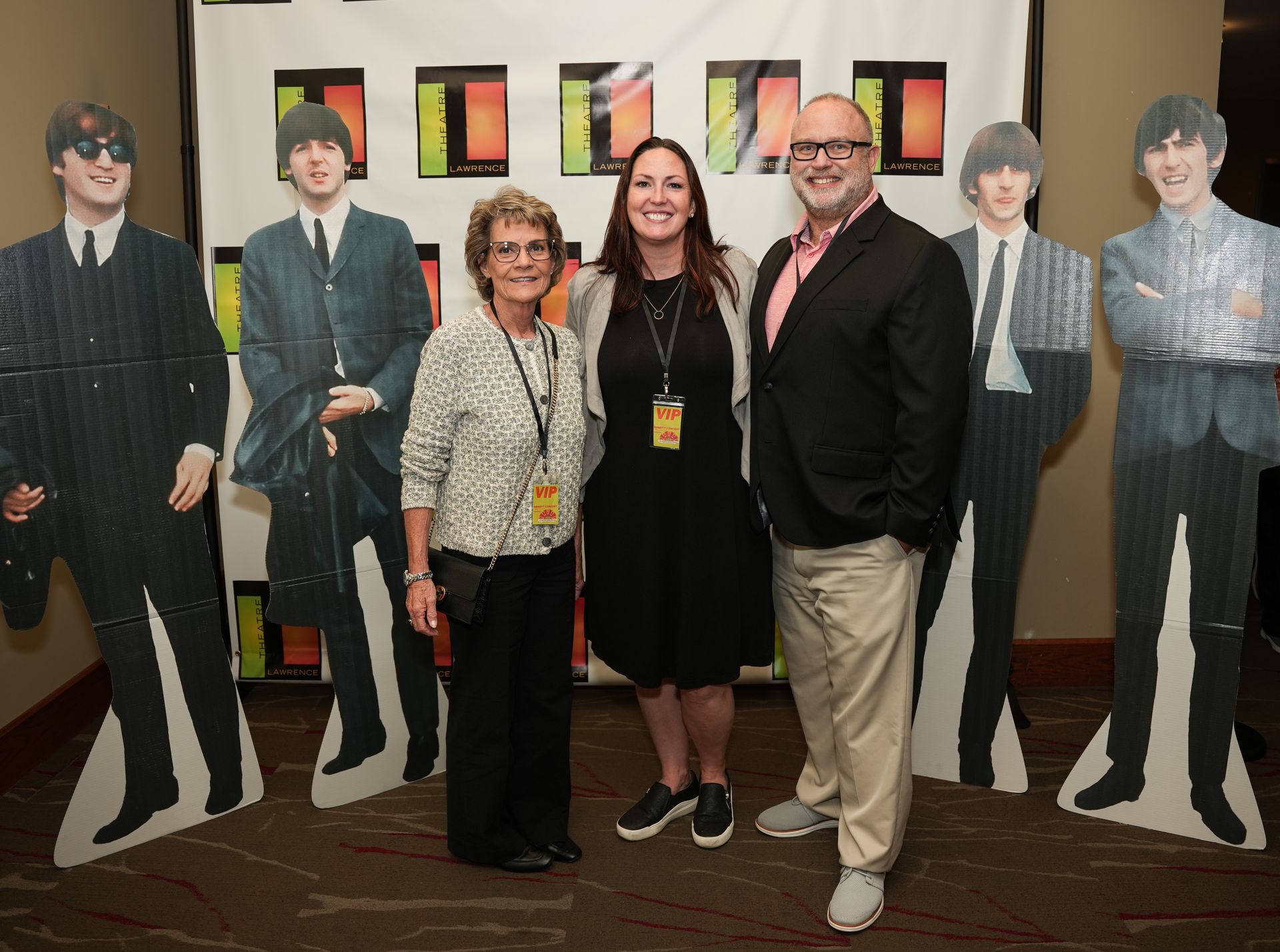 Three people pose with Beatles cutouts. They're in front of a backdrop with colorful squares.